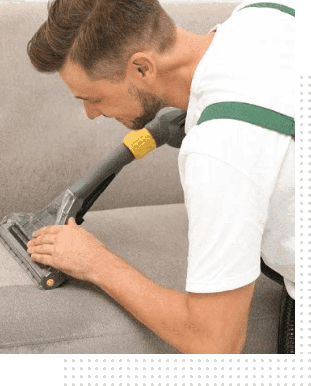 A man is using an electric vacuum to clean the couch.