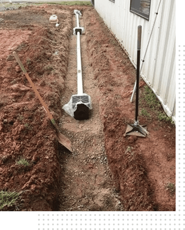 A pipe laying in the ground next to a fence.